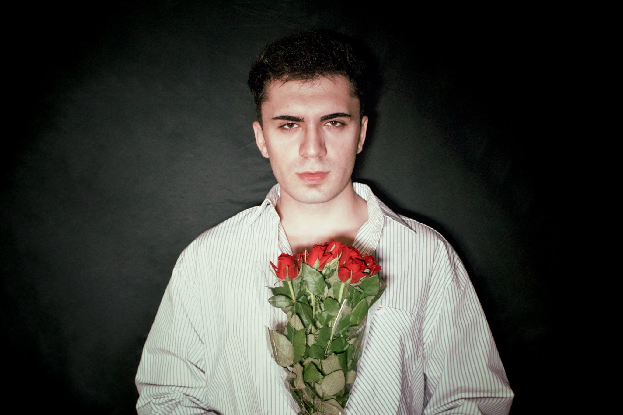 Pett Ruu holding a bouquet of red roses against a dark background